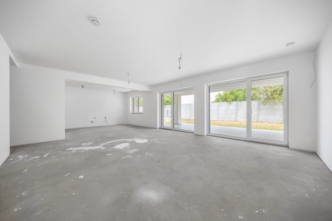 Living area before finishing: white walls, unfinished floor and large glazed doors to the terrace